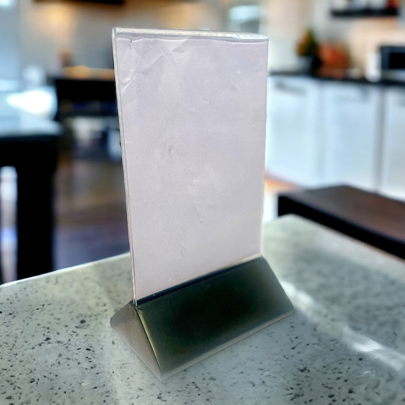 Skiltahaldari með A6 akrýl og svörtum plasti fót. 10,5 x 6,5 x H 19 cm.